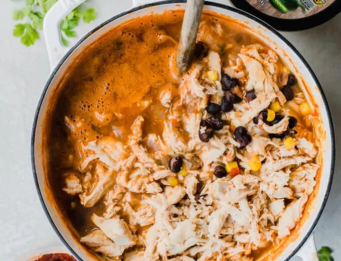 Large pot of chicken queso chili surrounded by fresh cilantro, onion, and cacique salsa and queso.