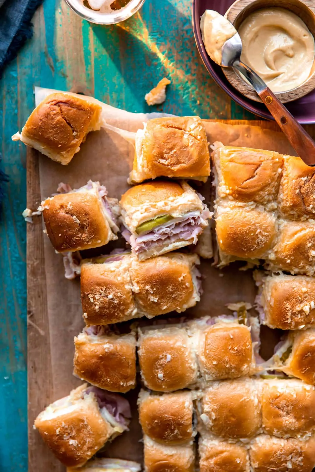 Overhead shot of a tray of cuban sliders that have been sliced apart, showing stretchy melty cheese attaching them.