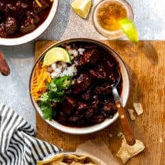 Overhead zeigt eine Tischdekoration mit hausgemachtem True Texas Chili, Schüsseln Chili serviert mit Tortilla Chips auf der Seite, Gläser Bier mit Limettenspalten und eine Flasche.