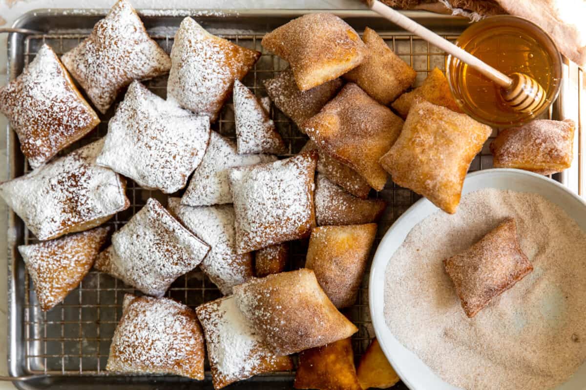 Sopapillas being dipped in cinnamon sugar and dusted with powdered sugar.