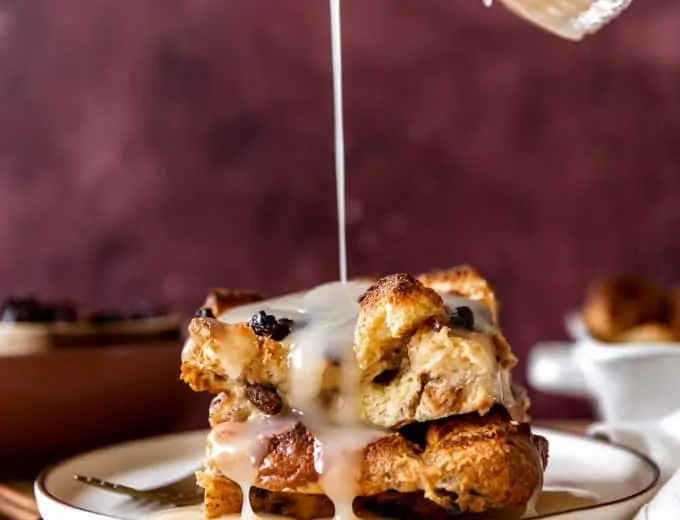 Vanilla syrup pouring over the top of a piece of bread pudding with raisins.