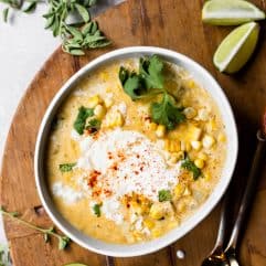 Bowl of Mexican Street Corn Chowder served with a swirl of Crema and crumbled queso fresco, lime wedges on the side.