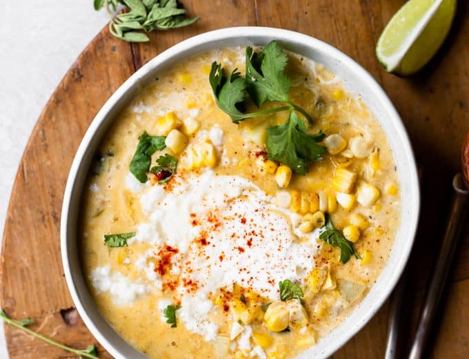 Bowl of Mexican Street Corn Chowder served with a swirl of Crema and crumbled queso fresco, lime wedges on the side.