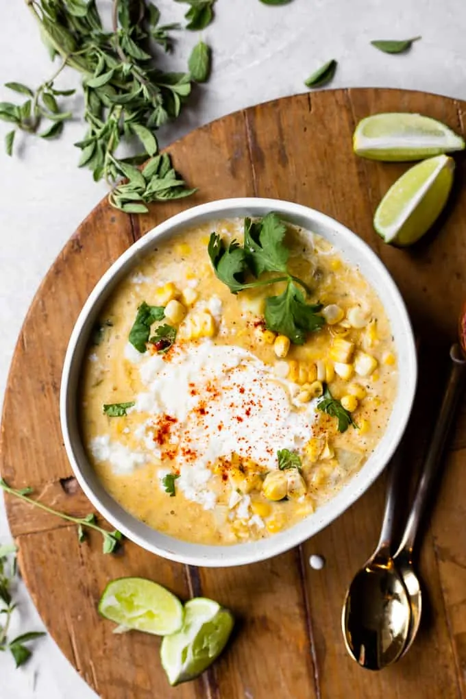 Bowl of Mexican Street Corn Chowder served with a swirl of Crema and crumbled queso fresco, lime wedges on the side. 