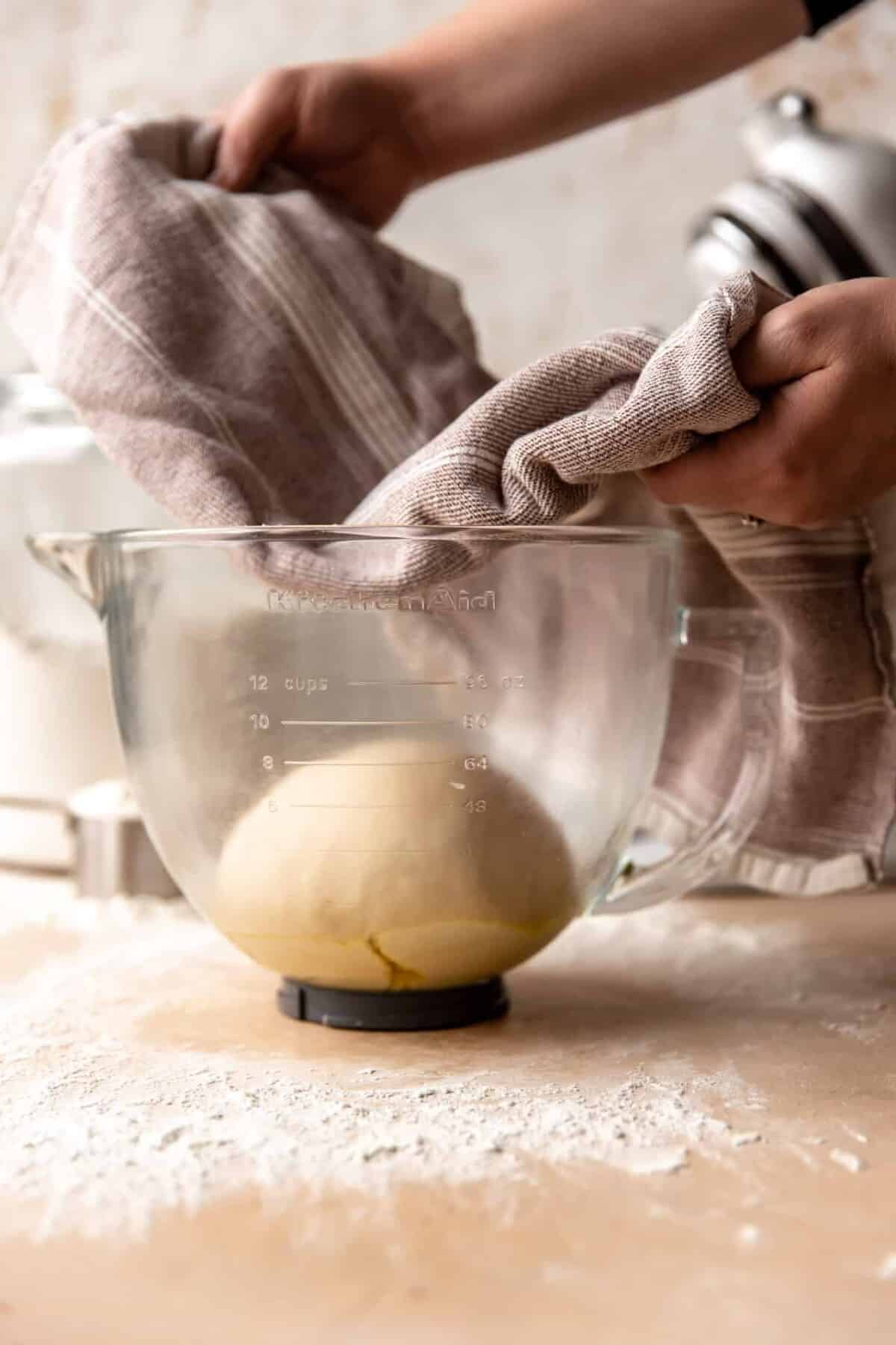 Dough in glass bowl being covered with a towel to allow rising time.