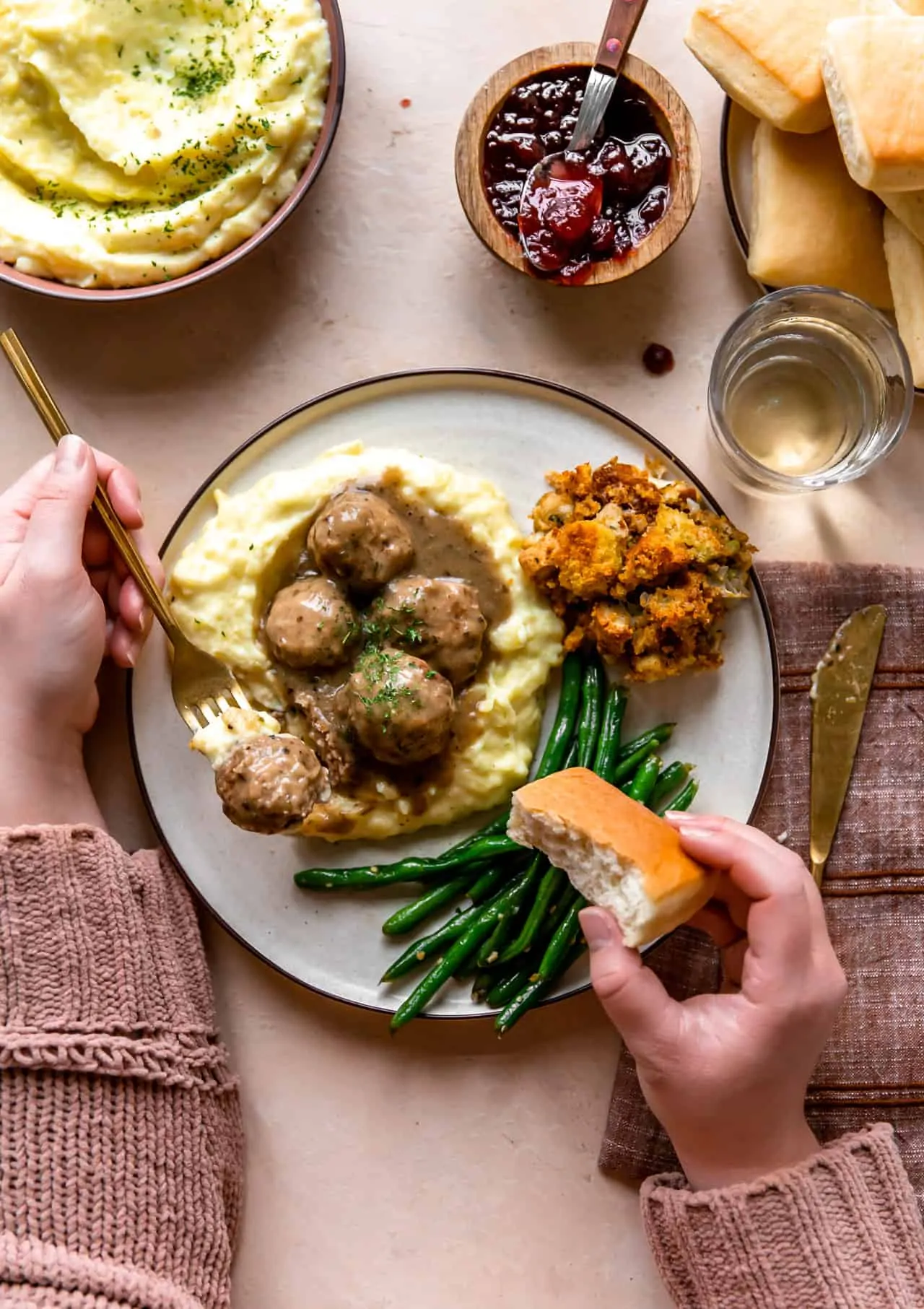 Hands around a plate of turkey meatballs served over mashed potatoes, bread rolls, green beans and stuffing. 