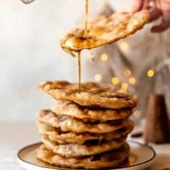 Piloncillo syrup drizzling over a stack of freshly fried bunuelos.