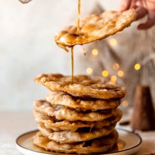 Piloncillo syrup drizzling over a stack of freshly fried bunuelos.