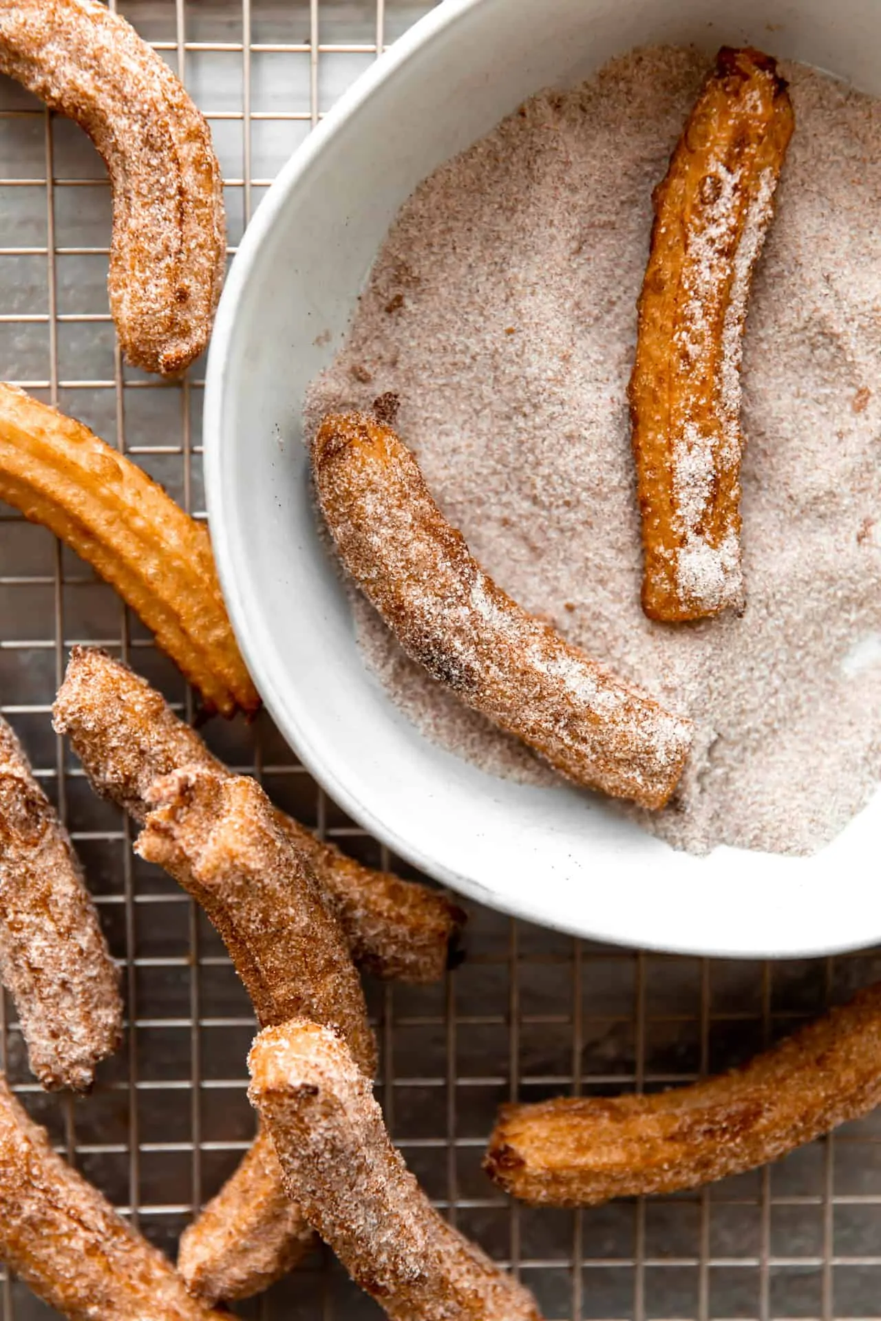 Fried churros being coated in cinnamon sugar mixture.