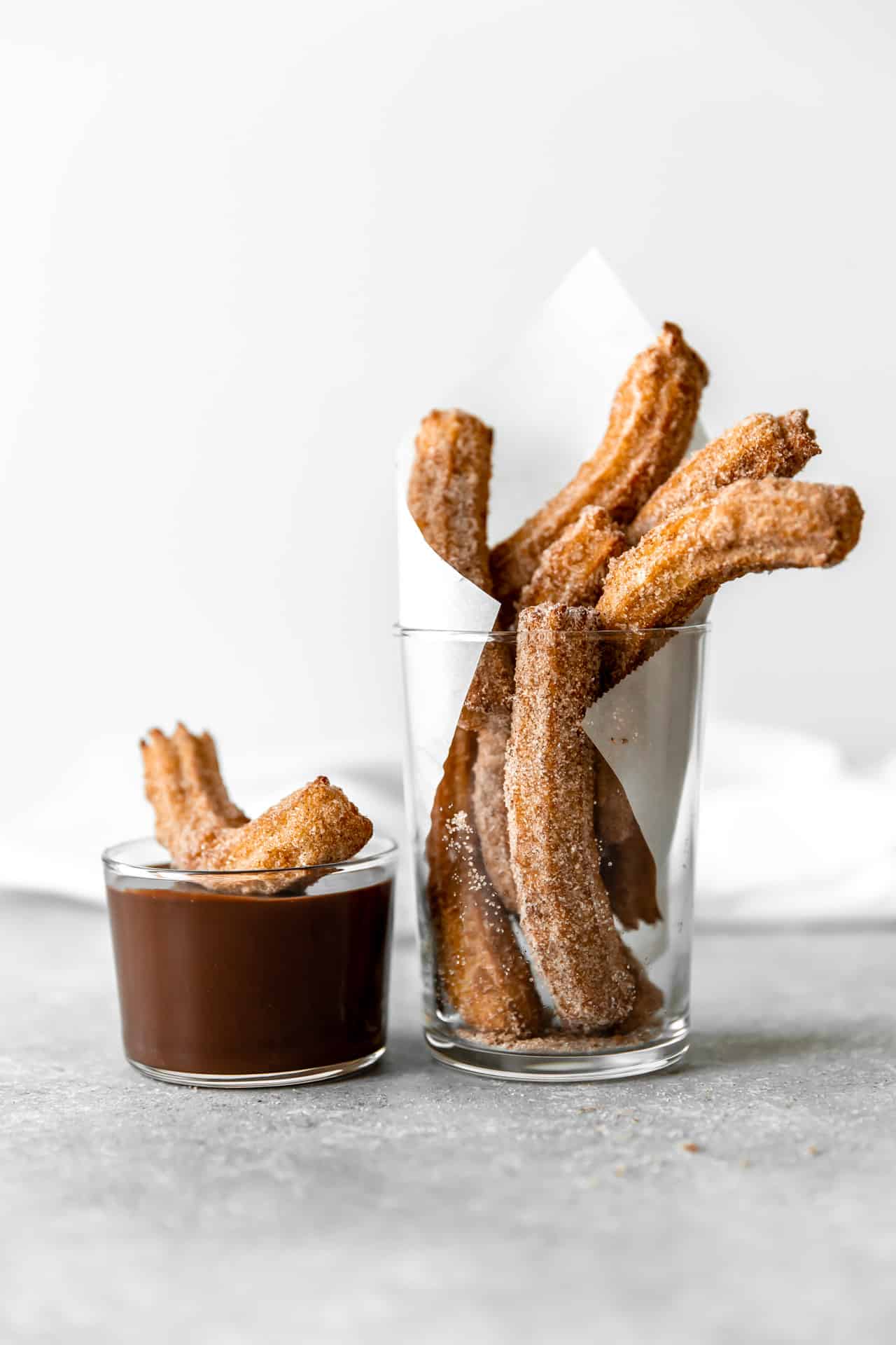 Fried Churros in a cup with a small cup of chocolate fudge sauce.