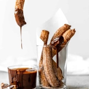 Churro being dipped into chocolate fudge.