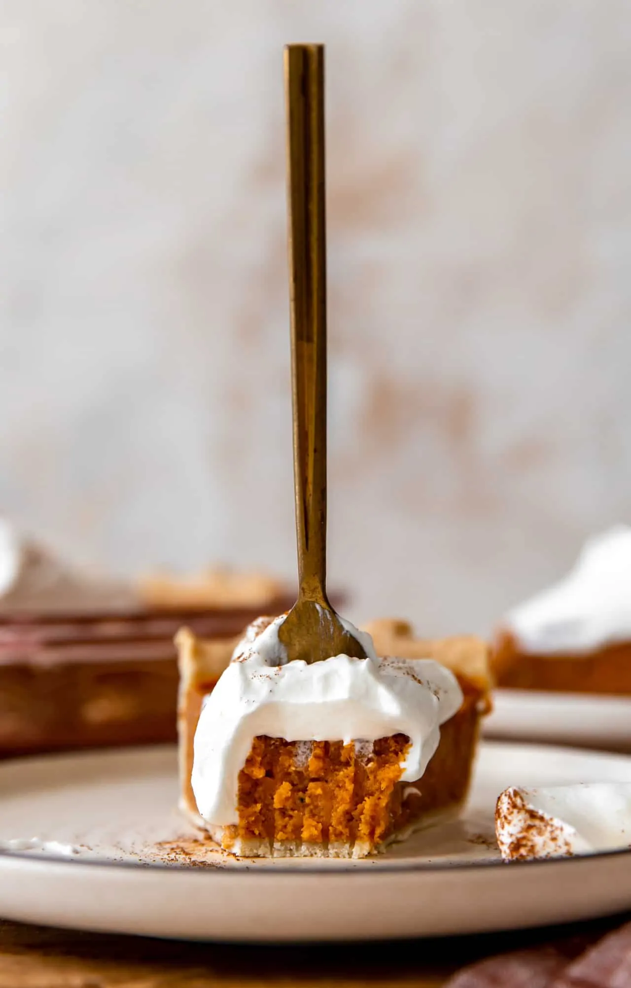 Front view of a slice of sweet potato pie with a bite missing and a fork sticking in the top.