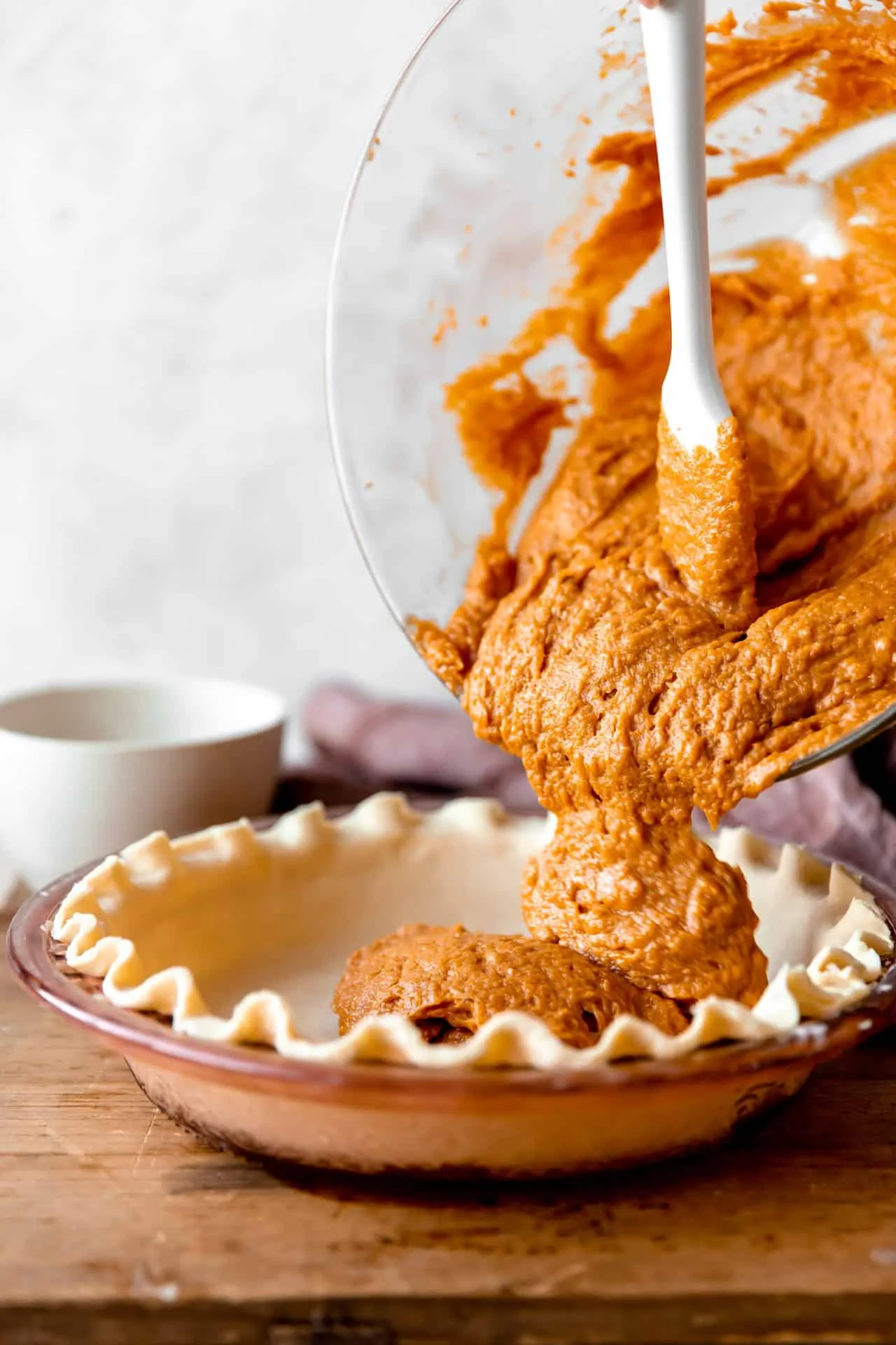 Homemade sweet potato pie filling being poured into a pie shell. 