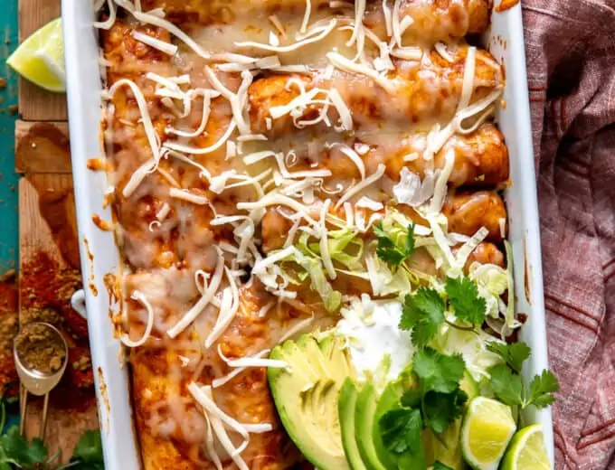 White baking dish filled with chicken enchiladas and topped with sliced avocado, sour cream and fresh cilantro.