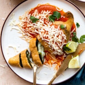 Plated Chile Rellenos with red sauce, sliced showing melted cheese inside.