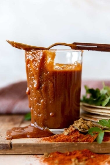 Cup filled with homemade enchilada sauce, with sauce dripping down the side and a spoon on top.