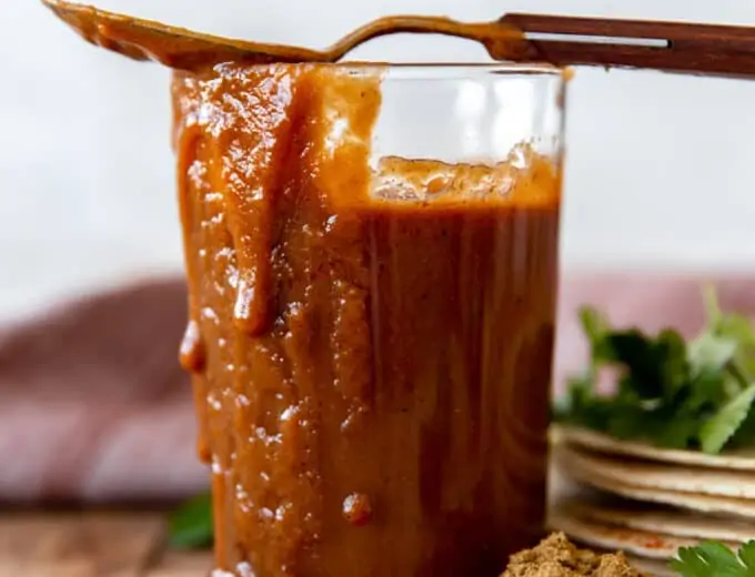 Cup filled with homemade enchilada sauce, with sauce dripping down the side and a spoon on top.