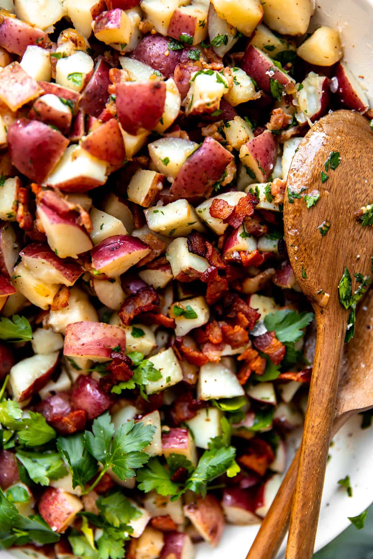 Up close of mixed together german potato salad with bits of bacon and garnished with fresh parsley.