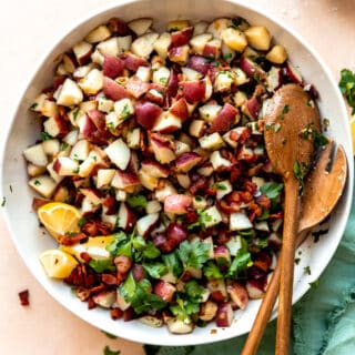 White bowl on a teal napkin, serving warm german potato salad with wooden spoons.
