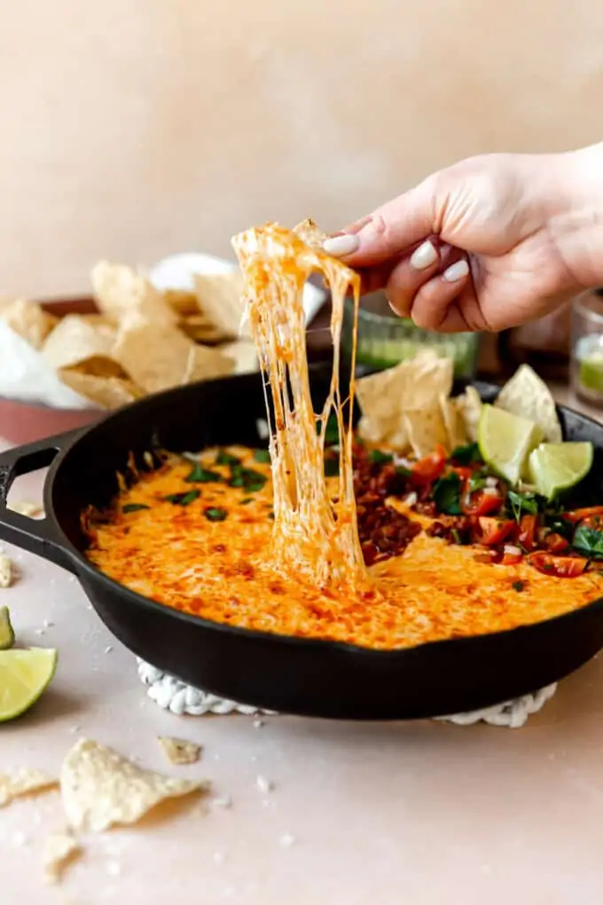 A chip dipping into a skillet of queso with chorizo.