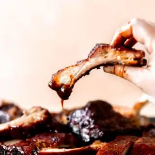 Hand picking up a smoked pork rib dipped in BBQ sauce.