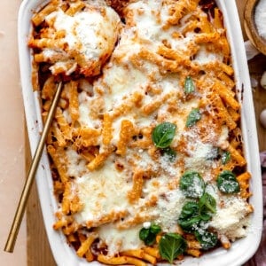Baked ziti in a baking dish served with a large spoon.