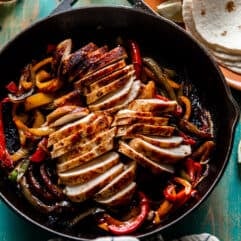Skillet filled with chicken fajitas with beers and flour tortillas on the side.