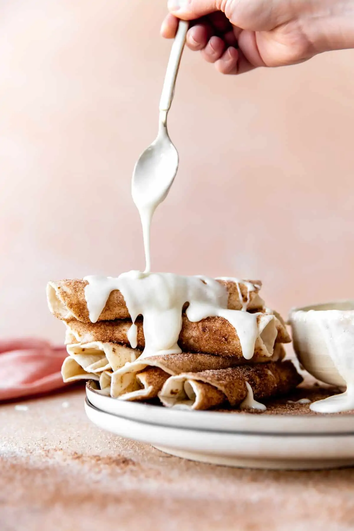Stack of cinnamon tortillas being drizzled with cream cheese glaze.
