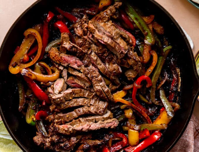 Large cast iron skillet filled with sliced grilled steak and grilled bell peppers and onions.