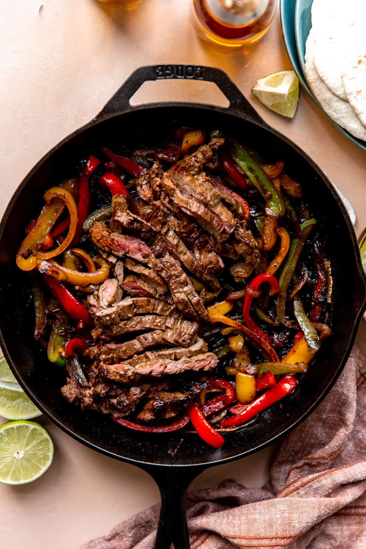 Large cast iron skillet filled with sliced grilled steak and grilled bell peppers and onions. 