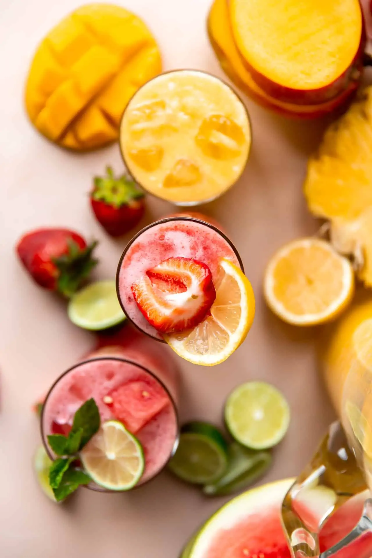 Overhead shot of cups of agua fresca on a counter surrounded by fruits. 