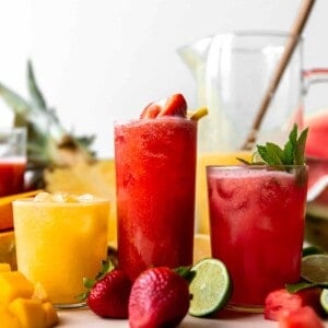 Glasses of agua fresca lined up showing strawberry, watermelon and a pineapple mango.