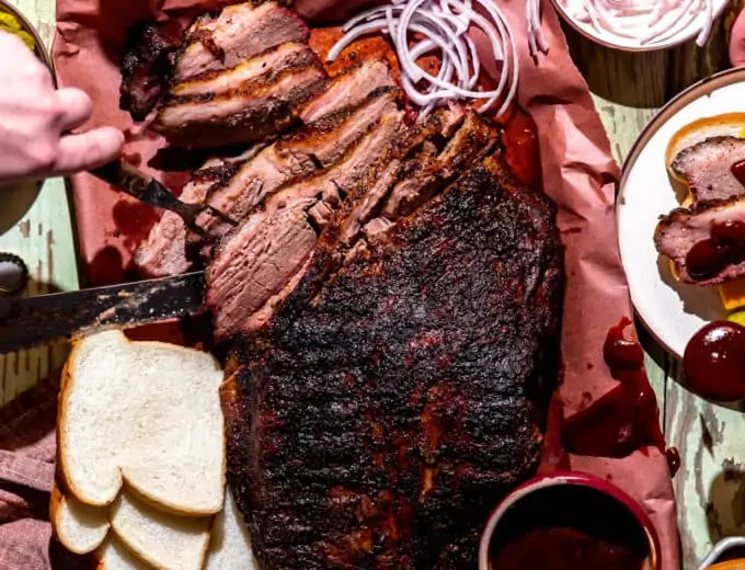 Texas Brisket on peach paper, sliced with slices of bread, cheese, pickles and onions around.