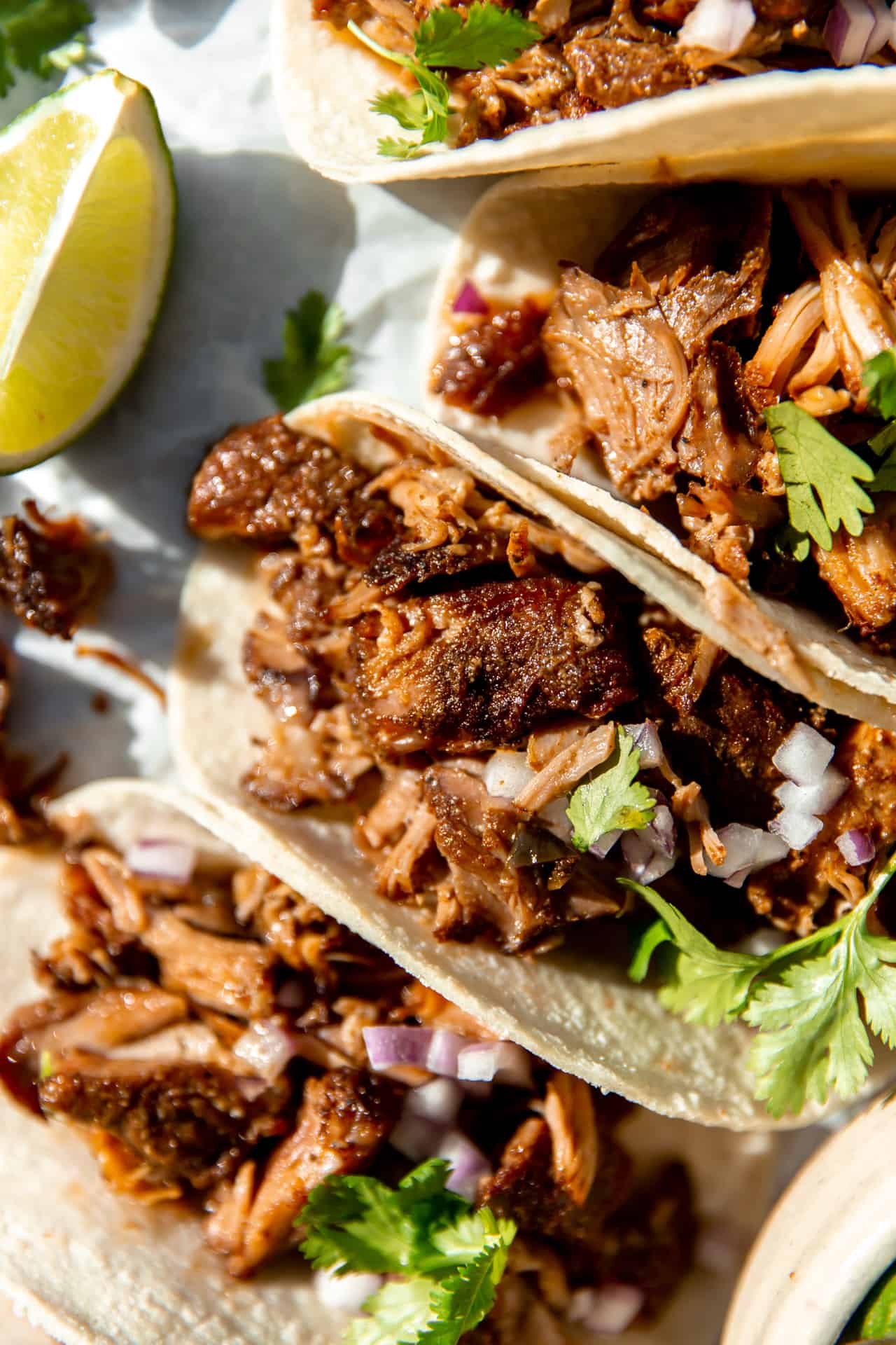 Up close view of carnitas tacos showing crispy pieces of pork in soft corn tortillas with cilantro and diced onion.