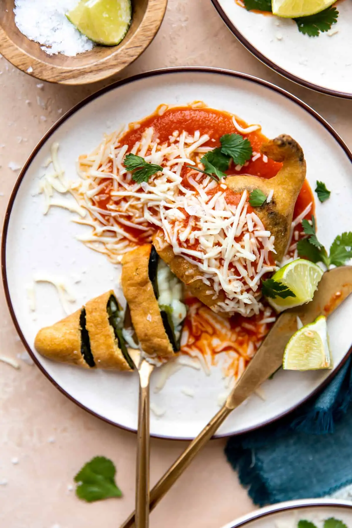 Plated Chile Rellenos with red sauce, sliced showing melted cheese inside.