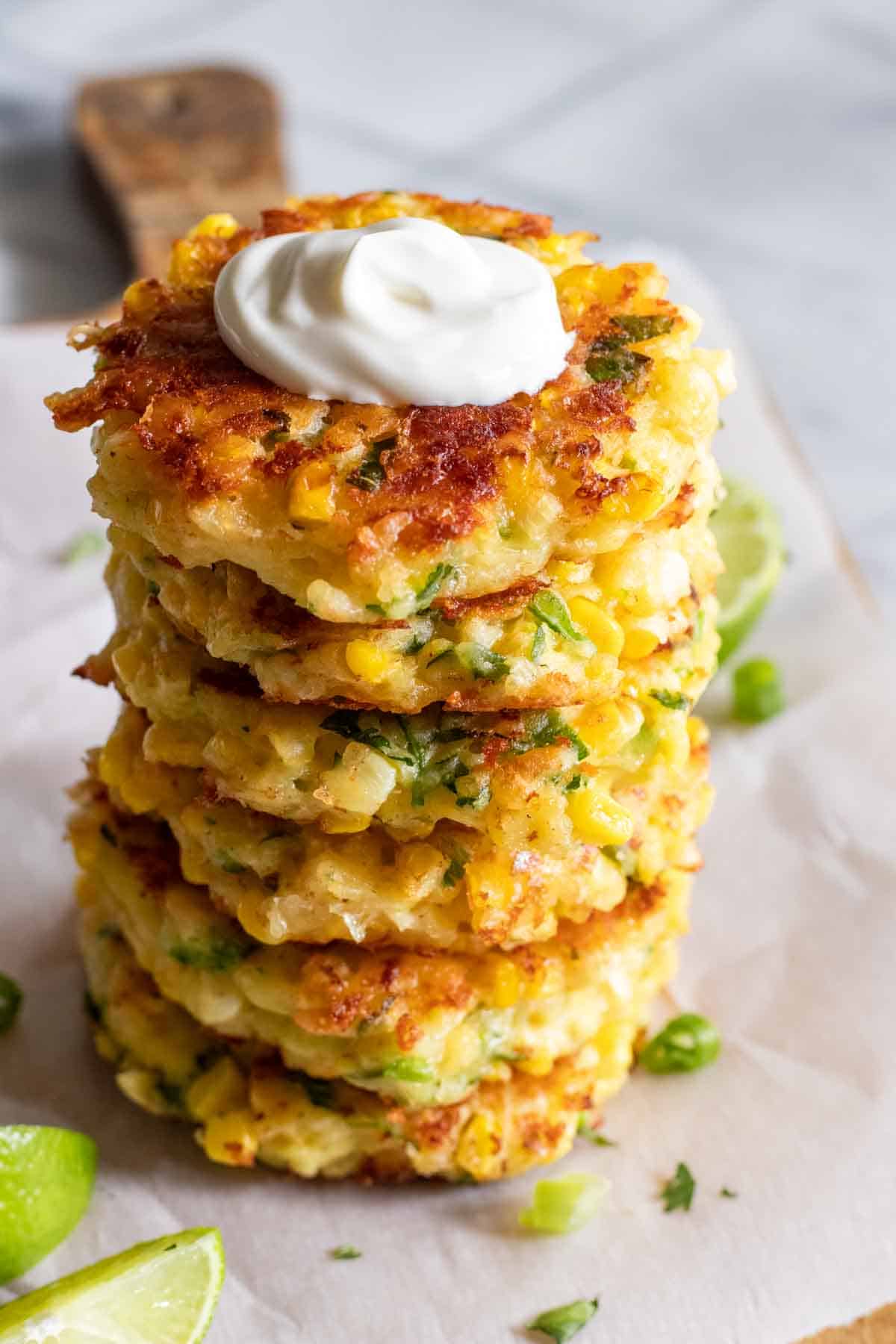 Stack of homemade corn fritters topped with a swirl of sour cream.