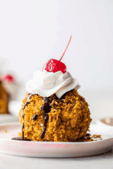 Fried Ice cream served on a plate, topped with whipped Cream and cherries