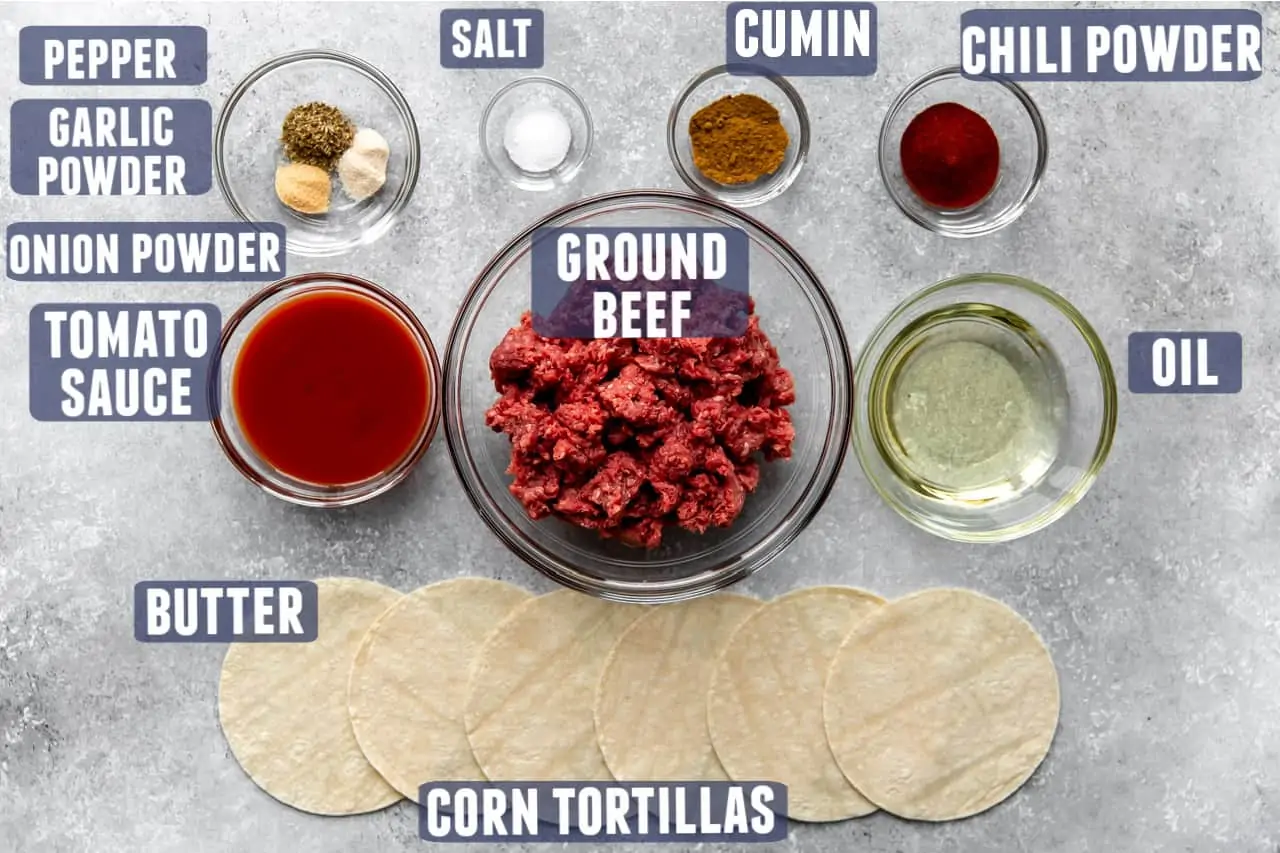 Ingredients needed to make ground beef taco meat and tacos laid on the counter.