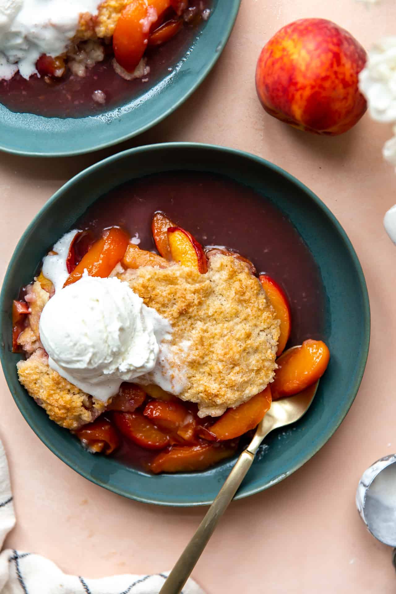 Peach cobbler with a crispy biscuit crust and a scoop of ice cream in a bowl.
