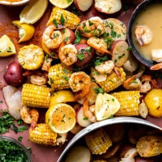 Shrimp boil spread out on butcher paper, with a side of old bay seasoning, beer and garlic butter.