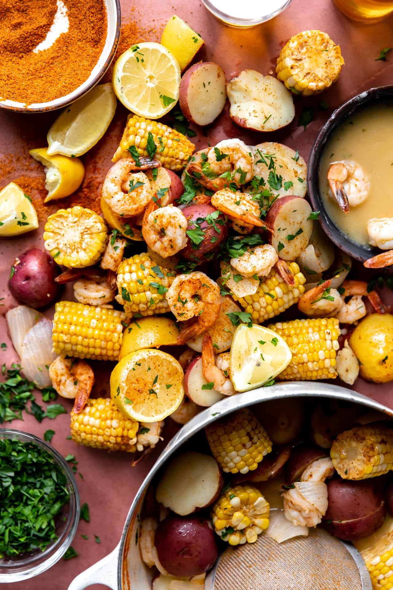 Shrimp boil spread out on butcher paper, with a side of old bay seasoning, beer and garlic butter.