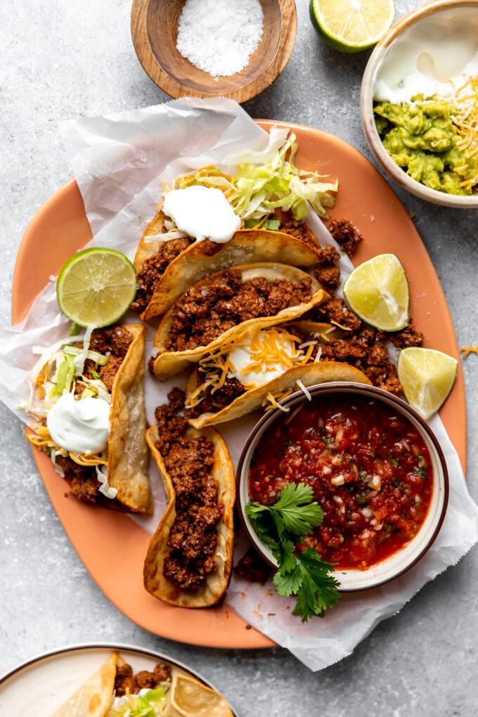 Plate filled with ground beef tacos with a bowl of salsa and guacamole on the side.