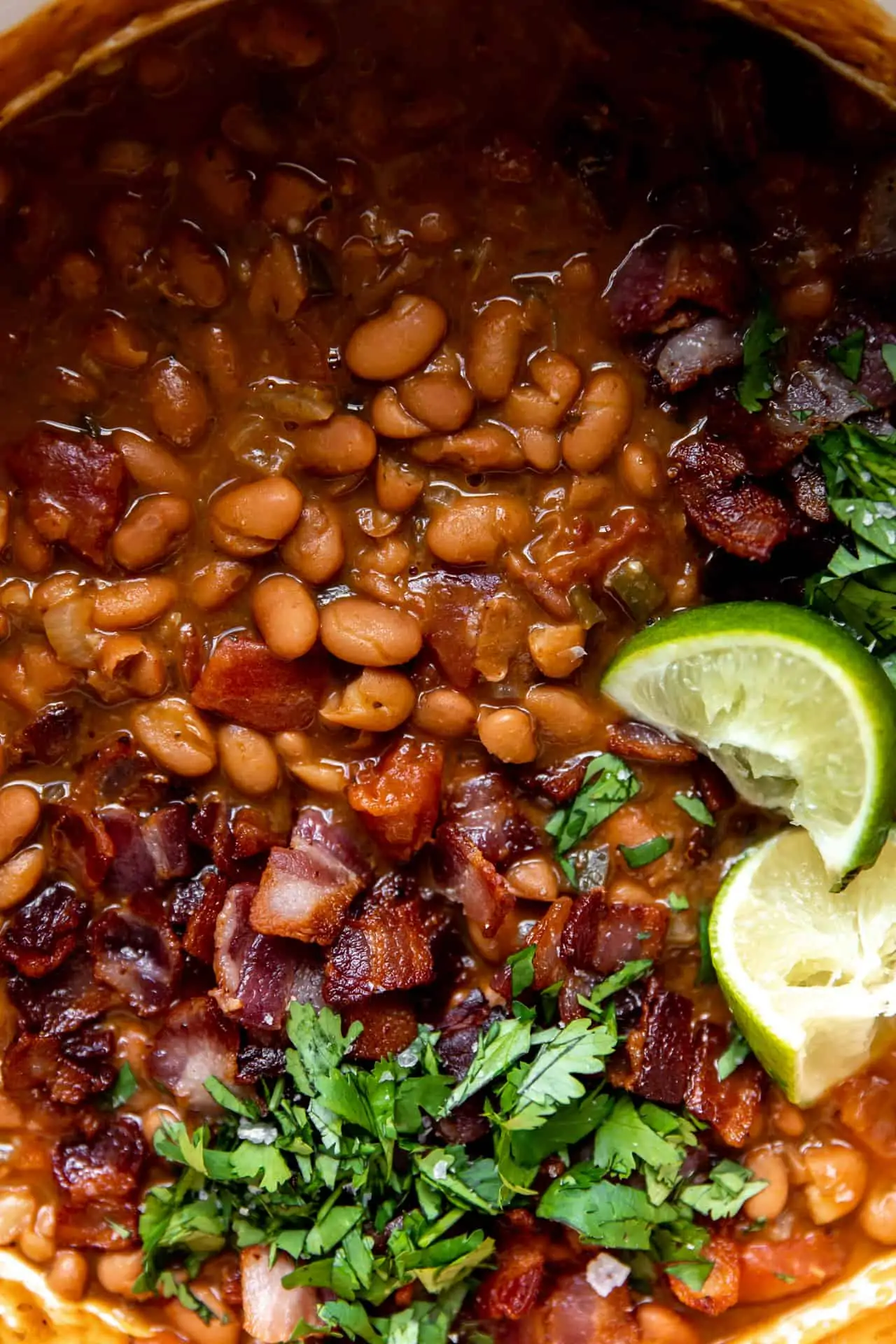 Up close view of cooked borracho beans topped with diced cilantro and lime wedges. 