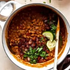 Dutch oven filled with cooked borracho beans topped with cilantro and lime wedges.