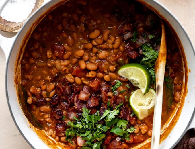 Dutch oven filled with cooked borracho beans topped with cilantro and lime wedges.