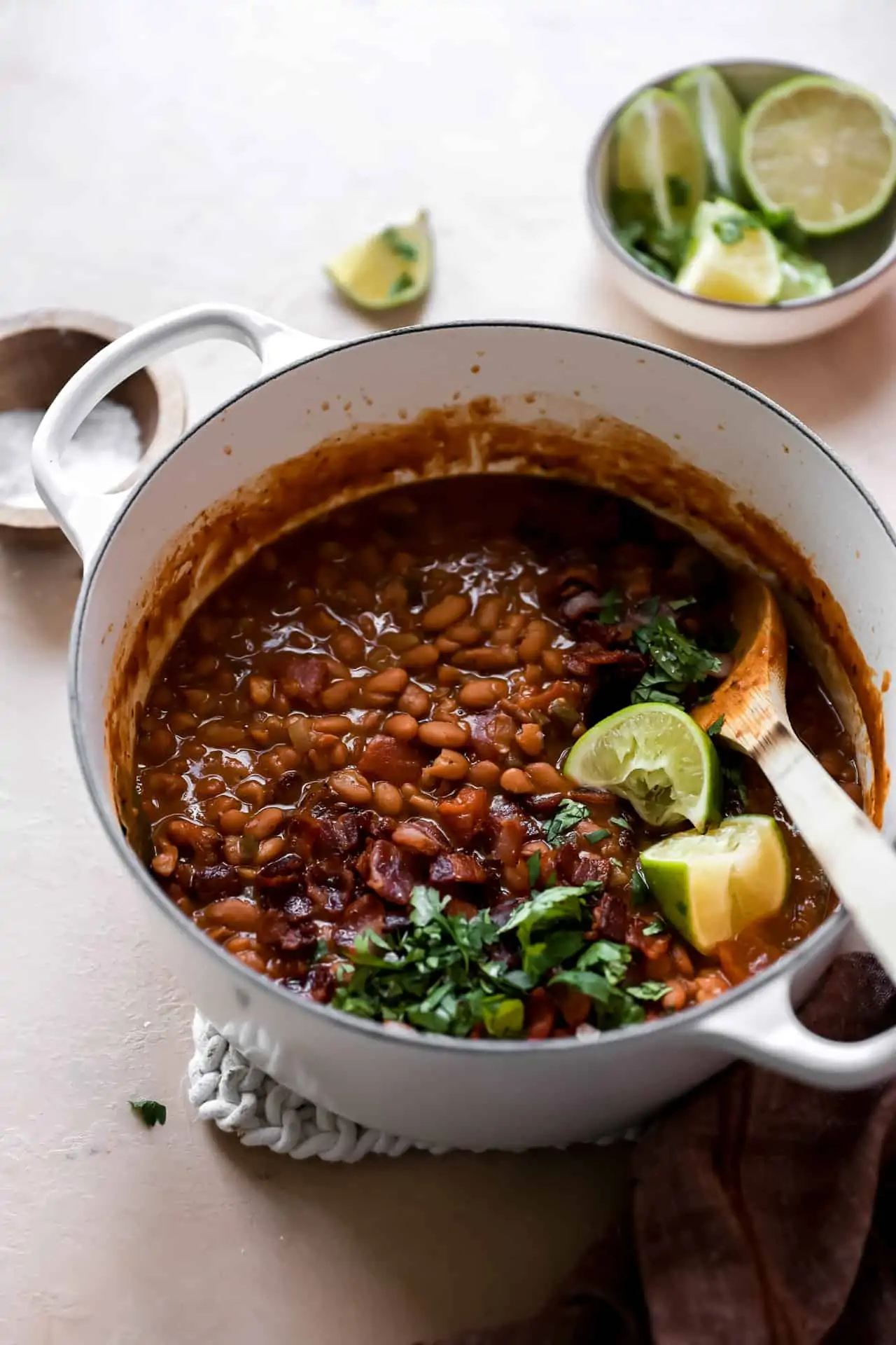 Pot filled with cooked borracho beans topped with cilantro and lime wedges.