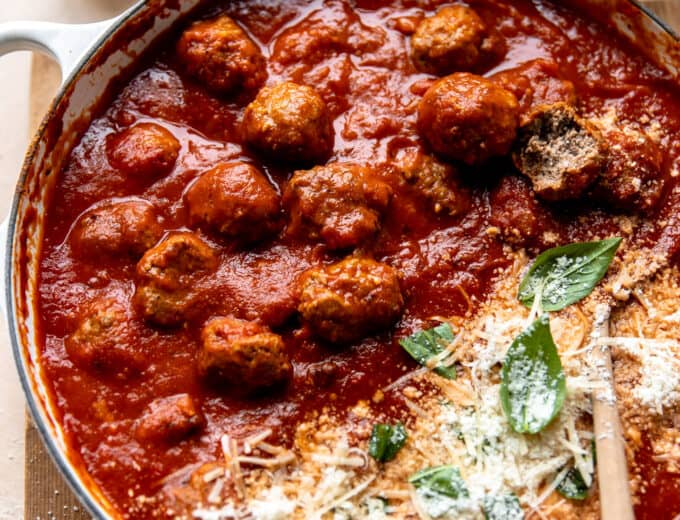 Skillet filled with meatballs cooked in sauce and topped with fresh parmesan and basil leaves.
