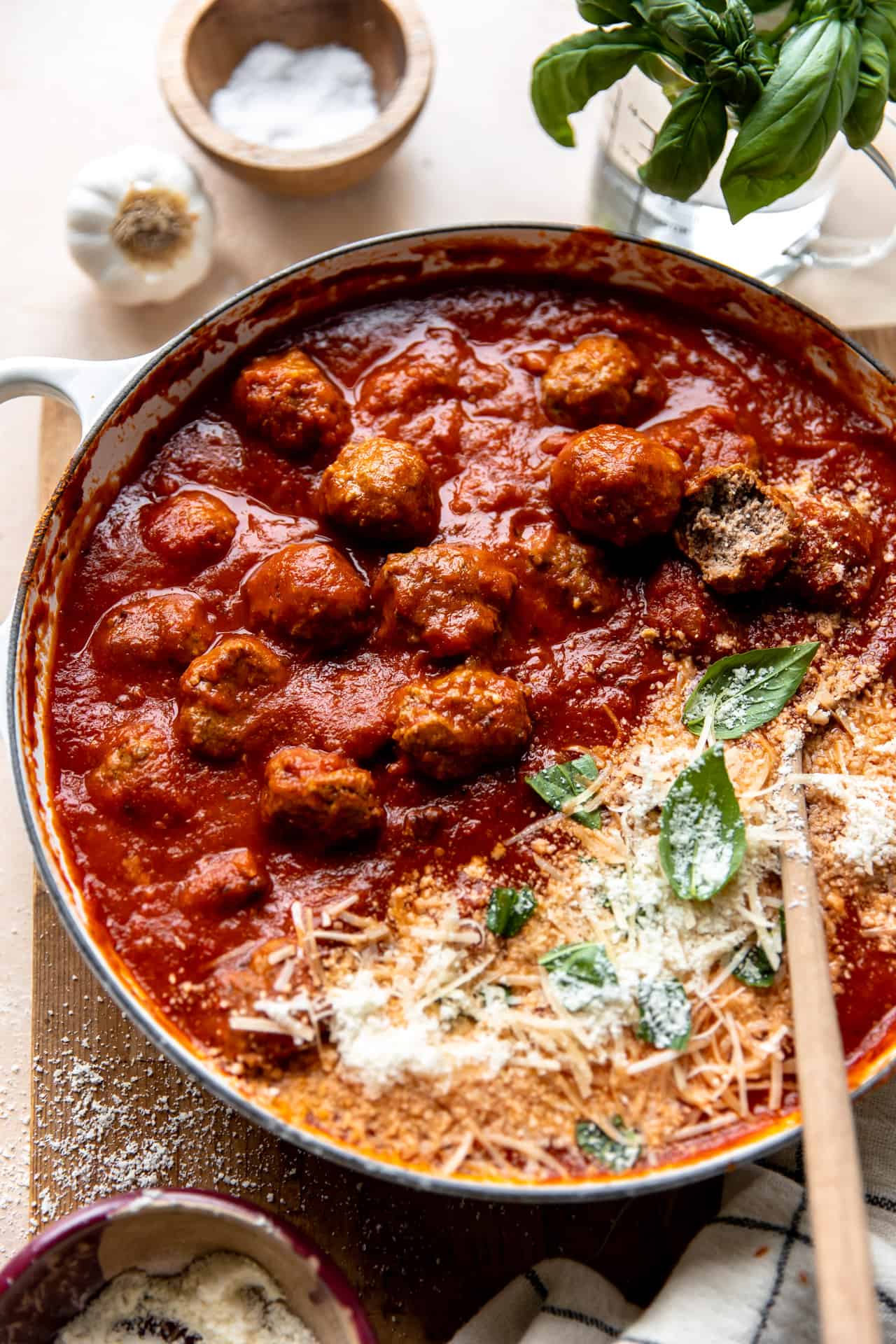 Skillet filled with meatballs cooked in sauce and topped with fresh parmesan and basil leaves.