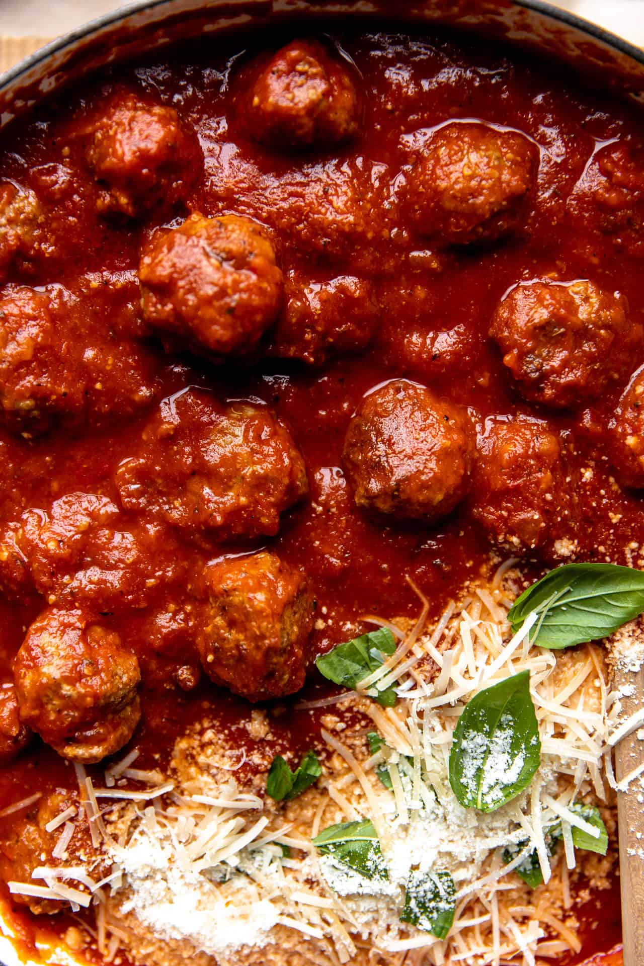 Up close view of meatballs simmered in red marinara sauce and topped with fresh parmesan.