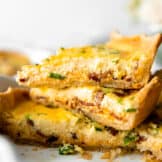 Sliced quiche stacked in a pie dish showing a custard egg filling and flakey pie crust.